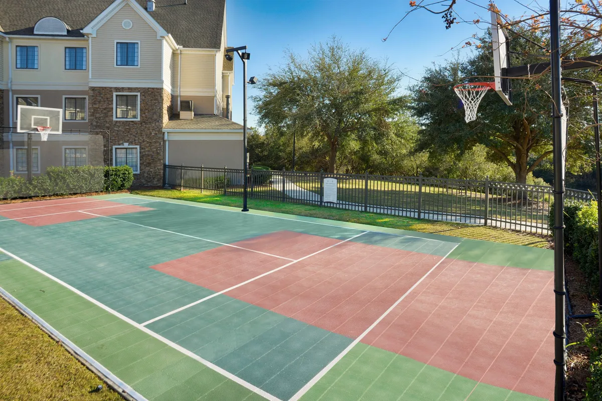 An energetic basketball court with a hoop, clearly marked court lines, and vibrant greenery surrounding the area. The space is open, active, and perfect for family-friendly sports and bonding.