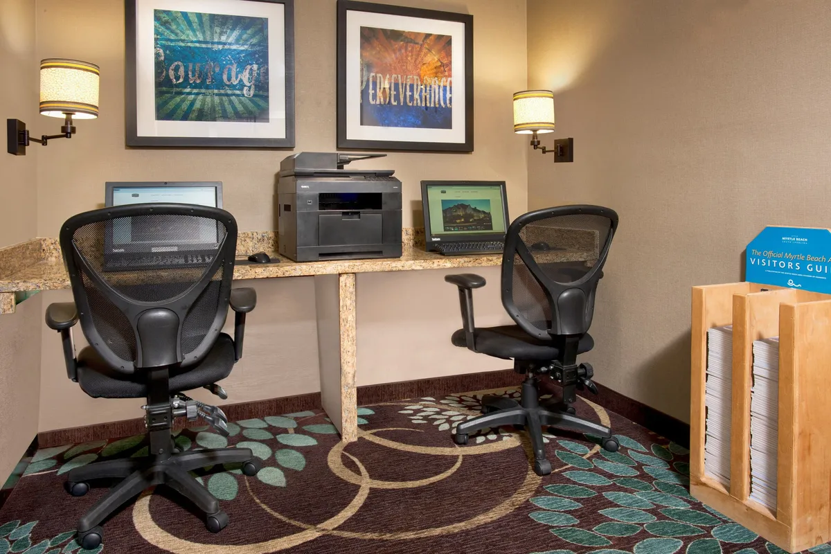This welcoming business lounge features computers, a printer, inspiring artwork, and a visitor guide display. The mood is productive yet inviting, ideal for guests who need to work or plan their stay.