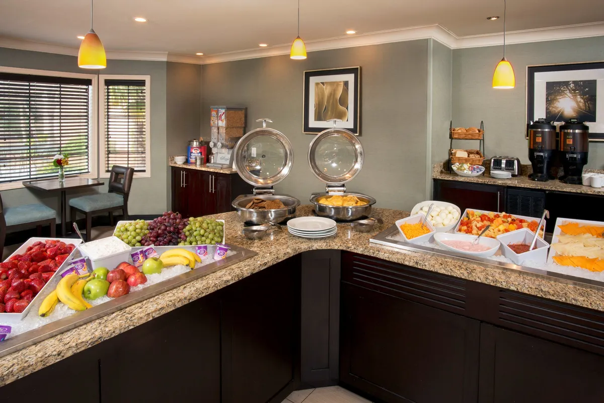 A welcoming breakfast buffet setup is shown, featuring fresh fruits, a coffee station, and a relaxed seating area. There’s an inviting atmosphere of socialization and leisurely starts to the day, with guests able to enjoy meals at their own pace.