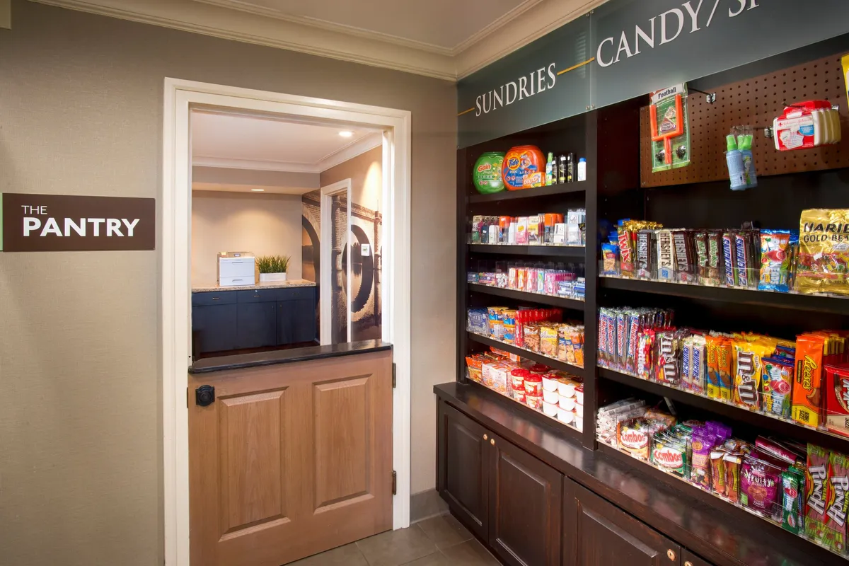 A cozy interior shot of 'THE PANTRY,' with well-stocked shelves of snacks and candies. The relaxed, convenient atmosphere invites guests to grab essentials or indulge in nostalgic treats. The space feels approachable and is ideal for picking up last-minute items or satisfying late-night cravings.